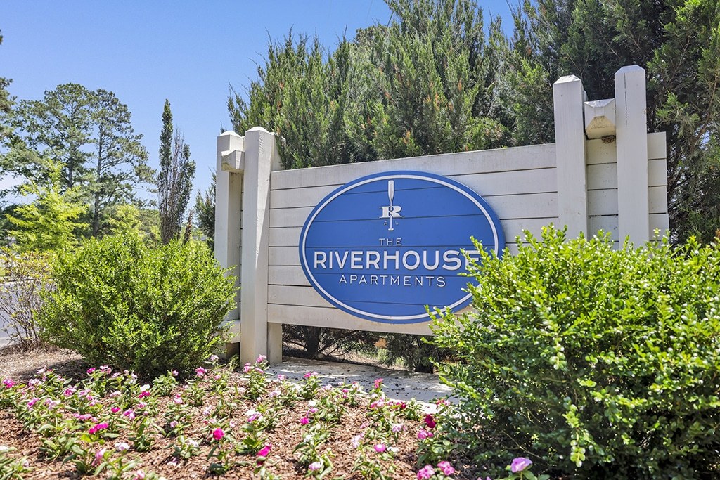 A sign for Riverhouse Apartments is surrounded by flowers and greenery.